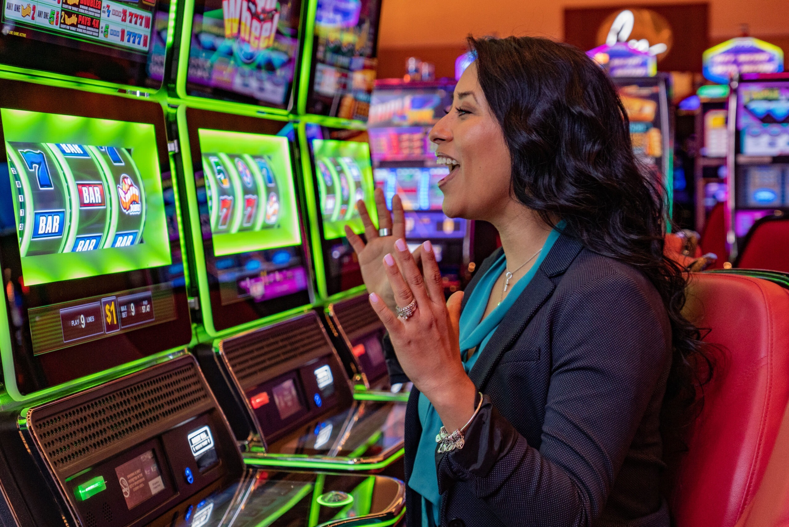 A woman excitedly looking on as she awaits for the slot machine to stop spinning