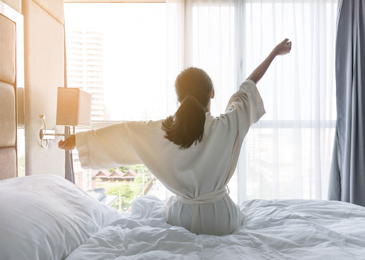 Woman waking up, arms stretched as the sun shines bright.